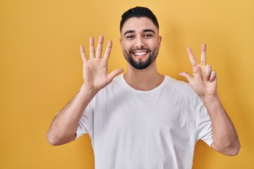 Wall Mural - Young handsome man wearing casual t shirt over yellow background showing and pointing up with fingers number eight while smiling confident and happy.