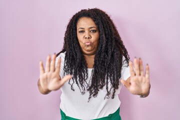 Poster - Plus size hispanic woman standing over pink background moving away hands palms showing refusal and denial with afraid and disgusting expression. stop and forbidden.