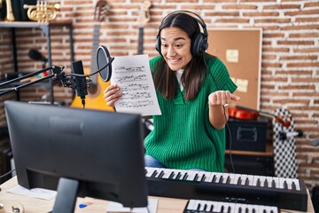 Poster - Young south asian woman doing online music tutorial showing music sheet screaming proud, celebrating victory and success very excited with raised arm