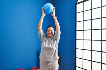Canvas Print - Middle age hispanic woman smiling confident stretching using ball at laundry room
