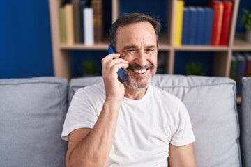 Wall Mural - Middle age man talking on smartphone sitting on sofa at home