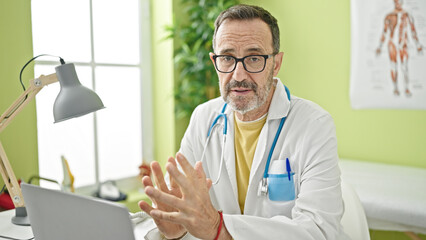 Canvas Print - Middle age man doctor using laptop speaking at clinic