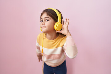 Little hispanic girl listening to music using headphones smiling with hand over ear listening and hearing to rumor or gossip. deafness concept.