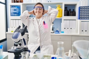 Poster - Hispanic girl with down syndrome working at scientist laboratory relaxing and stretching, arms and hands behind head and neck smiling happy