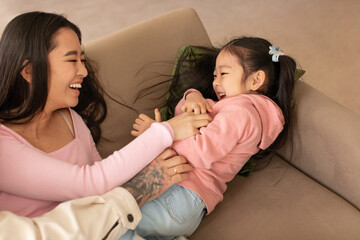 Wall Mural - Cheerful Chinese Woman Tickling Little Daughter And Laughing At Home