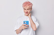 © WHstudio Leushin N - Pink haired European guy uses smartphone gaze fixated on screen fully engaged in app or absorbed in scrolling through social network showcasing determined concentrated approach to digital interaction