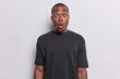 © wayhome.studio  - Black African man poses with shocked expression which conveys mix of astonishment and shock as if he just witnessed something truly remarkable stands speechless wears black t shirt isolated on white