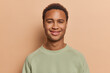 © wayhome.studio  - Portrait of handsome dark skinned African man smiles pleasantly being in good mood poses against brown background wears casual pullover. People emotions and happy feelings concept. Studio shot