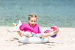 Adorable happy smiling little girl in pink t-shirt has fun with swimming ring unicorn on beach vacation. Happy summer vacation concept