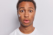 © WHstudio Leushin N - Close up shot of handsome middle aged dark skinned man applies face cream with care maintains healthy and nourished complexion keeps mouth opened stares impressed isolated over white background