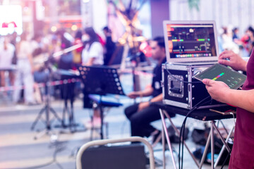 Selective focus to hand of sound engineer is tuning a sound system with blurry tablet smartdevice and musician in concert.