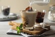 Pouring milk from jug into glass of delicious iced coffee, beans and mint on white wooden table