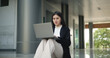© Johnstocker - Young Asian businesswoman in suit working on laptop while sitting on stairs