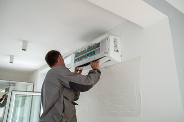 male worker wearing uniform installing air conditioner in apartment during summer season, man techni