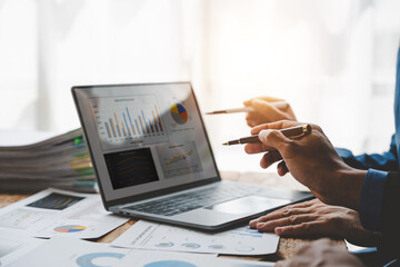 Young colleagues discuss business and analytical price charts using calculators and laptops to calculate financial, tax, accounting, statistics and analytical research ideas.