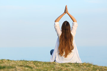 Wall Mural - Woman practicing yoga on the grass looking the horizon