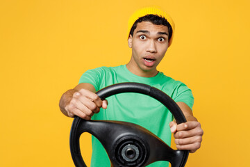 Wall Mural - Young scared man of African American ethnicity wears casual clothes green t-shirt hat hold steering wheel driving car look aside isolated on plain yellow background studio portrait. Lifestyle concept.