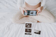 Cropped young pregnant woman wear pyjamas taking photo of ultrasound examination on mobile cell phone resting relax spend time in bedroom lounge home. Maternity family pregnancy expectation concept.