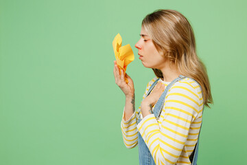 Wall Mural - Side view sick ill allergic woman has red watery eyes runny stuffy sore nose suffer from allergy trigger symptom hay fever hold napkin sneeze isolated on plain pastel green background studio portrait