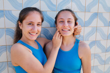 Happy Girl Touching Face Of Sister In Front Of Wall
