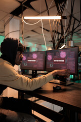 African american spy looking at hacking alert on multiple screens, planning security breach to steal personal information or passwords. Young adult using trojan virus and computer malware.