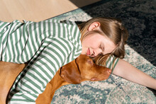 Girl Lying Down With Dog On Carpet At Home On Sunny Day