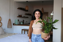 Smiling Young Woman Holding Potted Peace Lily At Home