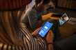 © Westend61 - Young woman operating electric car charging app on smart phone and man using laptop in background