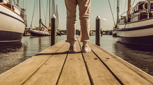 Legs Of A Man Standing On The Pier Against The Background Of Ships And Boats. Selective Focus, Close-up, Ground Level Shot. AI Generated