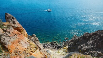 Wall Mural - Yacht sailing near the sea coast. Santorini island, Greece. Clear blue sea and red volcanic rocks. Summer seascape. Travel and vacation concept. 
