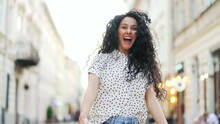 Attractive young hispanic curly woman walking on city street, she turns to camera and smiles Outdoor portrait happy female tourist having good time wandering around town in summer Come here, follow me