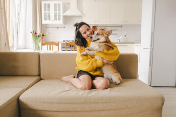 A brunet girl in a yellow sweater hugs a dog sitting on the couch 