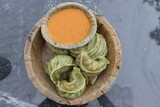 Fototapeta Krajobraz - Top view of the Hot green vegan Momo dumplings Dim Sum served with spicy schezwan sauce on a round wooden plate.