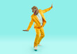 Happy man in dinosaur disguise skateboarding and having fun. Full length body portrait joyful man wearing bright yellow suit and funny reptile mask riding on pretend skateboard on turquoise background