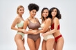 © LIGHTFIELD STUDIOS - Cheerful multicultural girlfriends in colorful and modern lingerie hugging each other and standing isolated on grey, different body types and self-acceptance, multicultural representation