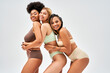 © LIGHTFIELD STUDIOS - Cheerful young african american woman in lingerie hugging friends and looking at camera while posing isolated on grey, different body types and self-acceptance concept, multicultural models