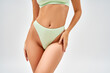 © LIGHTFIELD STUDIOS - Cropped view of sexy young woman in light green bra and panties touching hip while standing and posing isolated on grey, self-acceptance and body positive concept