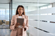 Young professional African American business woman company manager sales executive wearing suit holding fintech tab digital tablet computer standing in office at work, looking at camera, portrait.