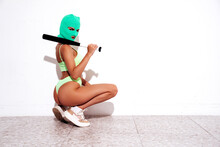Beautiful Sexy Woman In Green Underwear. Model Wearing Bandit Balaclava Mask. Hot Seductive Female In Nice Lingerie Posing Near White Wall In Studio. Crime And Violence. Holds Baseball Bat
