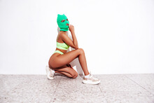 Beautiful Sexy Woman In Green Underwear. Model Wearing Bandit Balaclava Mask. Hot Seductive Female In Nice Lingerie Posing Near White Wall In Studio. Crime And Violence. Sits On The Floor