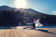 © olezzo - Caucasian middle-aged woman in a white shirt and swimsuit sitting on the pier against the backdrop of the mountains enjoying the summer sunset