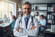 © FutureStock - Portrait of mature male doctor wearing white coat with stethoscope standing in class room office with students in the background.