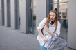 Hurry stressed blonde woman in white shirt outside business center looking anxious as things slip from her hands. She juggles a phone, take away late and book. Bewildered girl look at phone, confused.