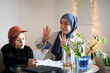 © Johnér - Mother wearing hijab holds up fingers while helping son doing math homework