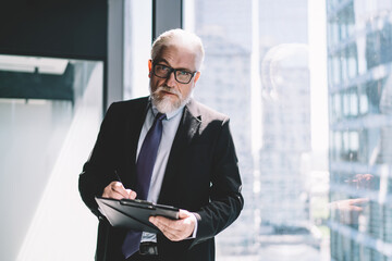 Sticker - Senior businessman standing with clipboard near glass wall