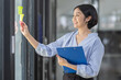 © David - Young Creative business asian woman writing on sticky notes on a glass wall, female colleague looking.