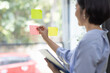 © David - Young Creative business asian woman writing on sticky notes on a glass wall, female colleague looking.