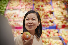 Smiling Woman In Supermarket Holding Red And Yellow Apple