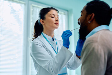 Wall Mural - Female doctor examining throat of black man during appointment at medical clinic.