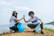 © eakgrungenerd - Man and woman volunteers cheerful hand touch high five holding rubbish bags. clean up garbage in tourist attractions. Conservation and care cleanliness in nature.